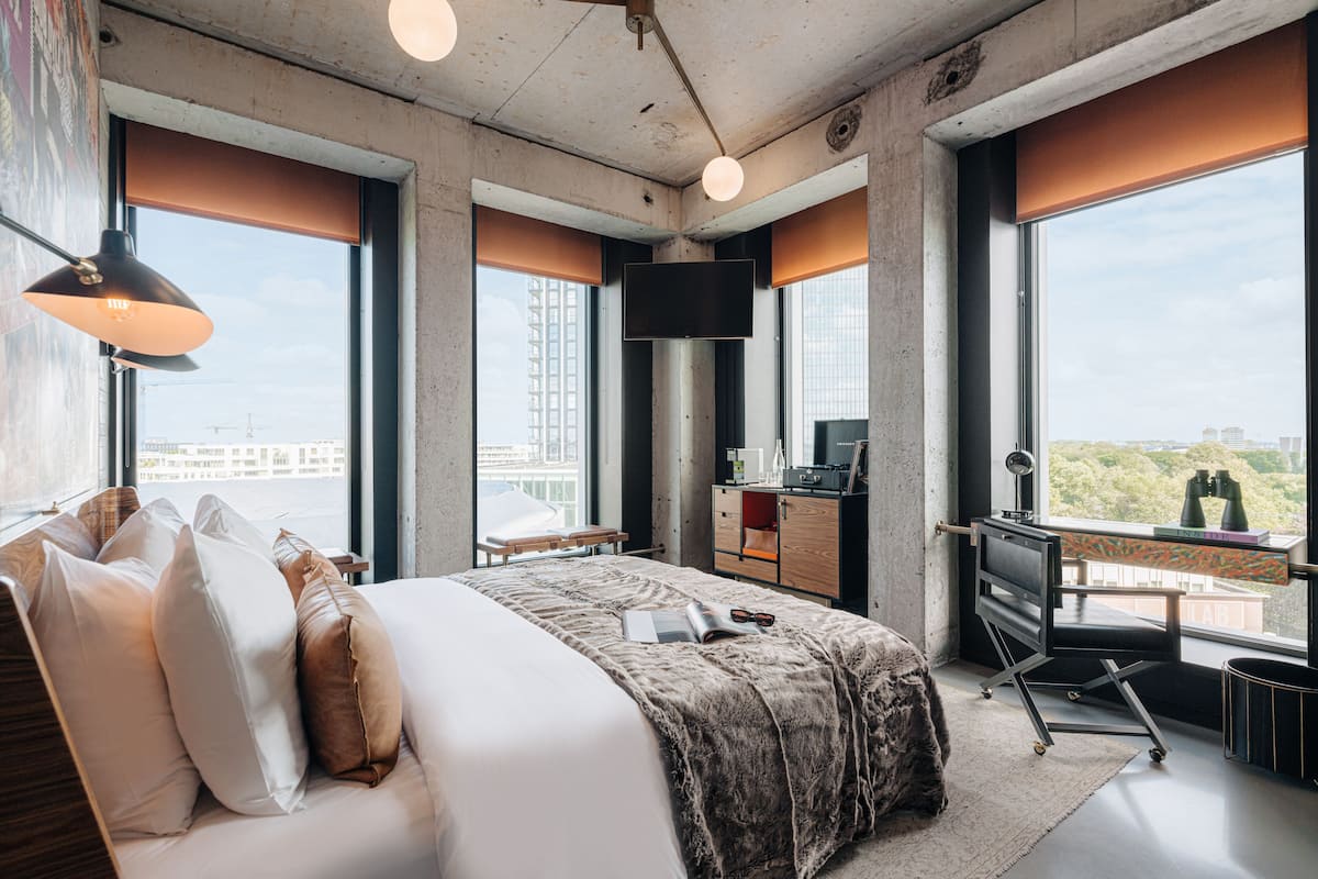A modern hotel room with a large bed, a desk with a computer, and a view of the city.