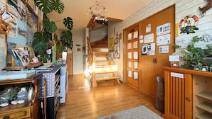 A hotel lobby with wooden floors, a staircase, and a reception desk with various items and plants. - Pension Natsumi no Sato (Biei)