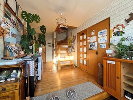 Vestíbulo de hotel con pisos de madera, una escalera y una recepción con objetos y plantas varios.