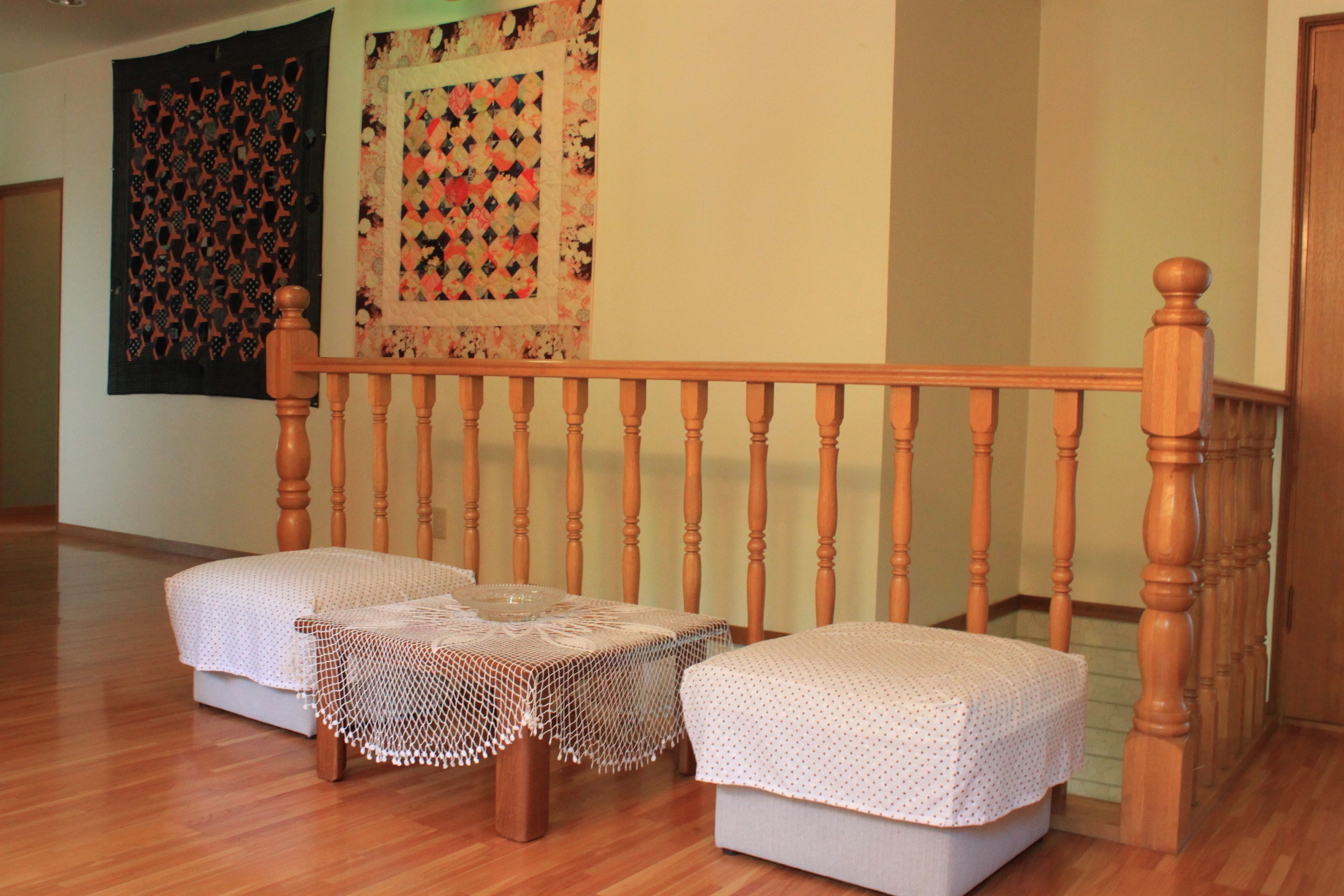 A staircase with a wooden handrail and a carpeted landing area with two cushioned seating and a small table.