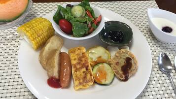 Un plato con varios alimentos, incluyendo maíz, salchicha, tortilla y ensalada.