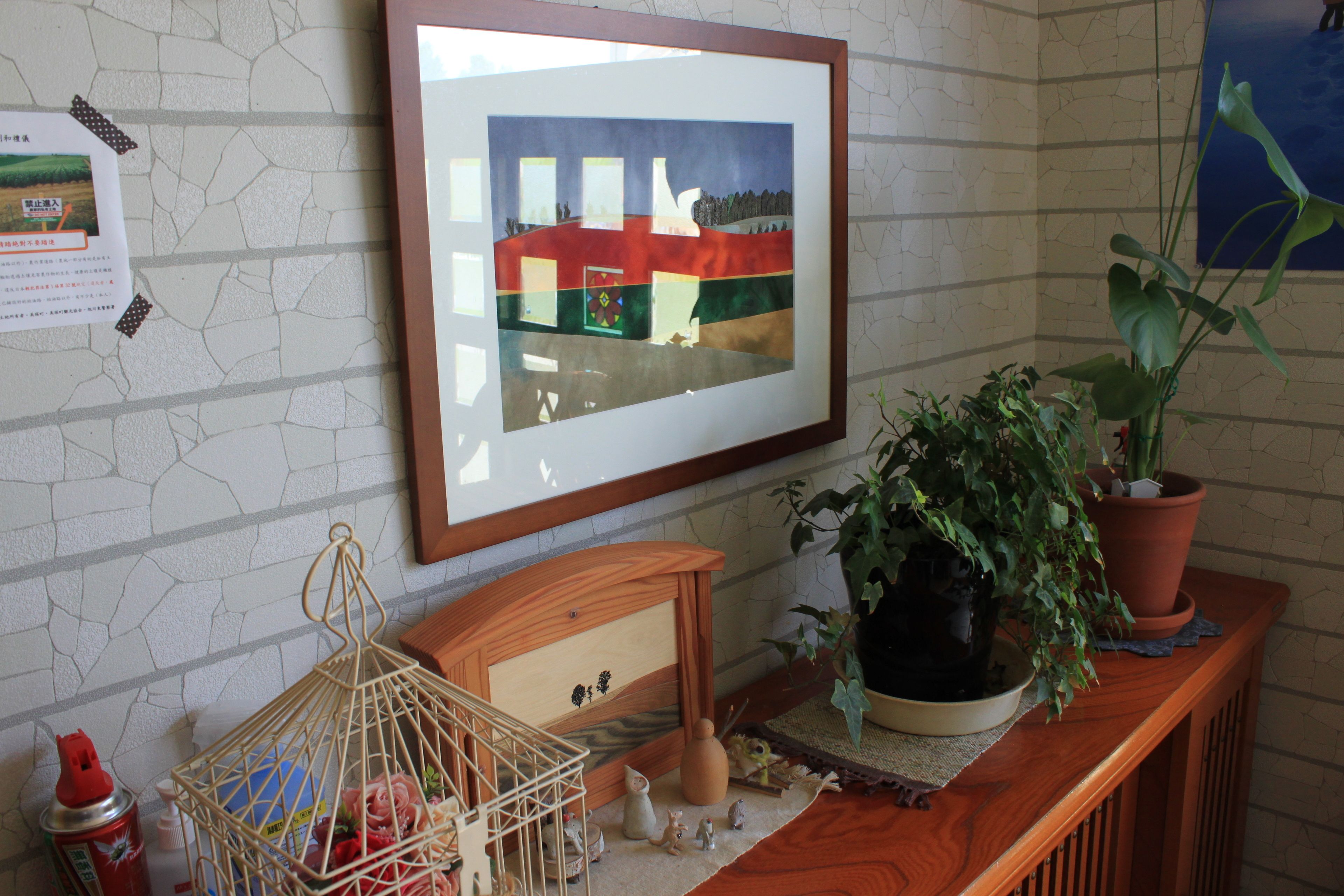 A framed artwork on a wall, a wooden cabinet with decorative items, and a potted plant on a wooden surface.