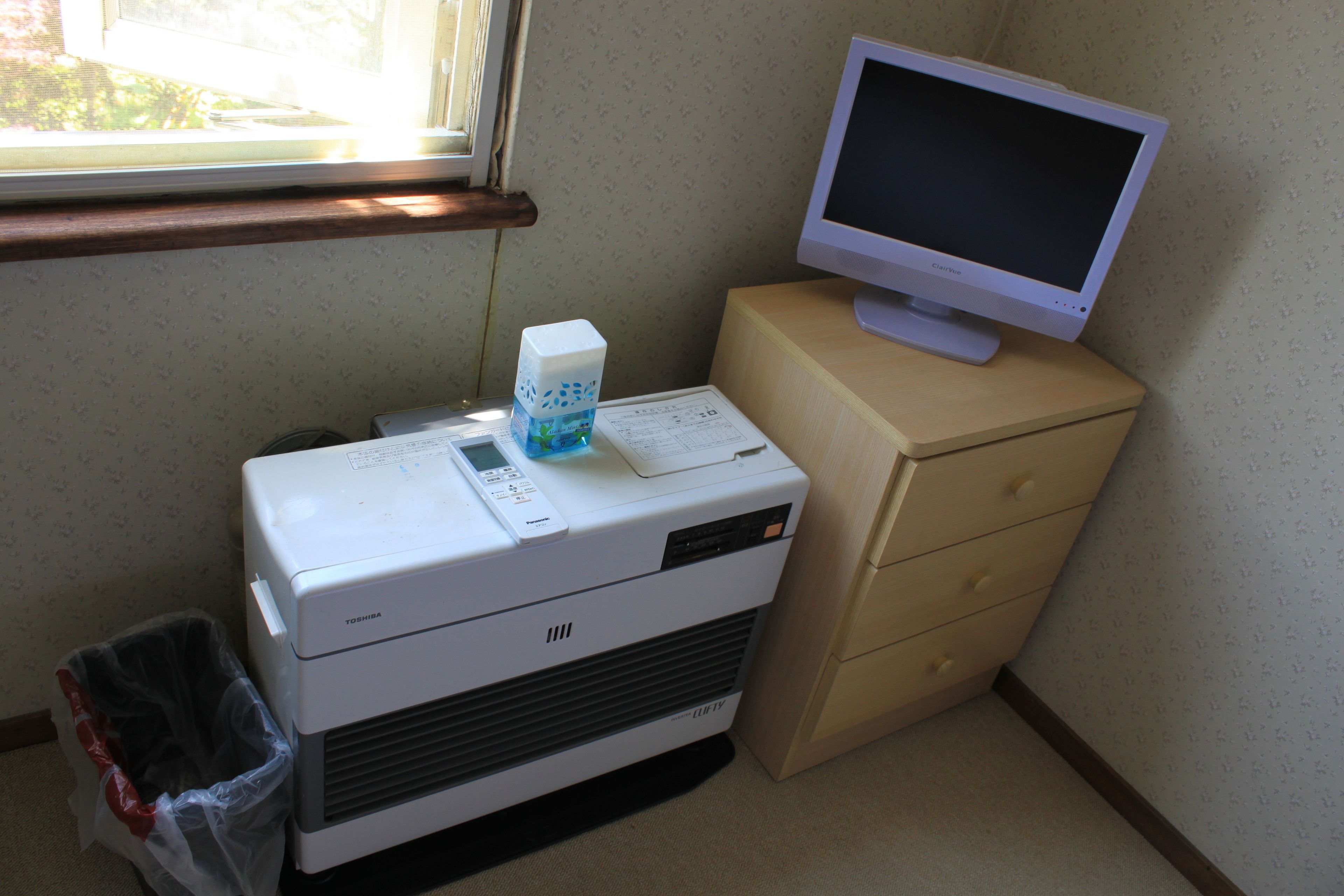 A room with a printer, a computer monitor on a cabinet, and a window with blinds.