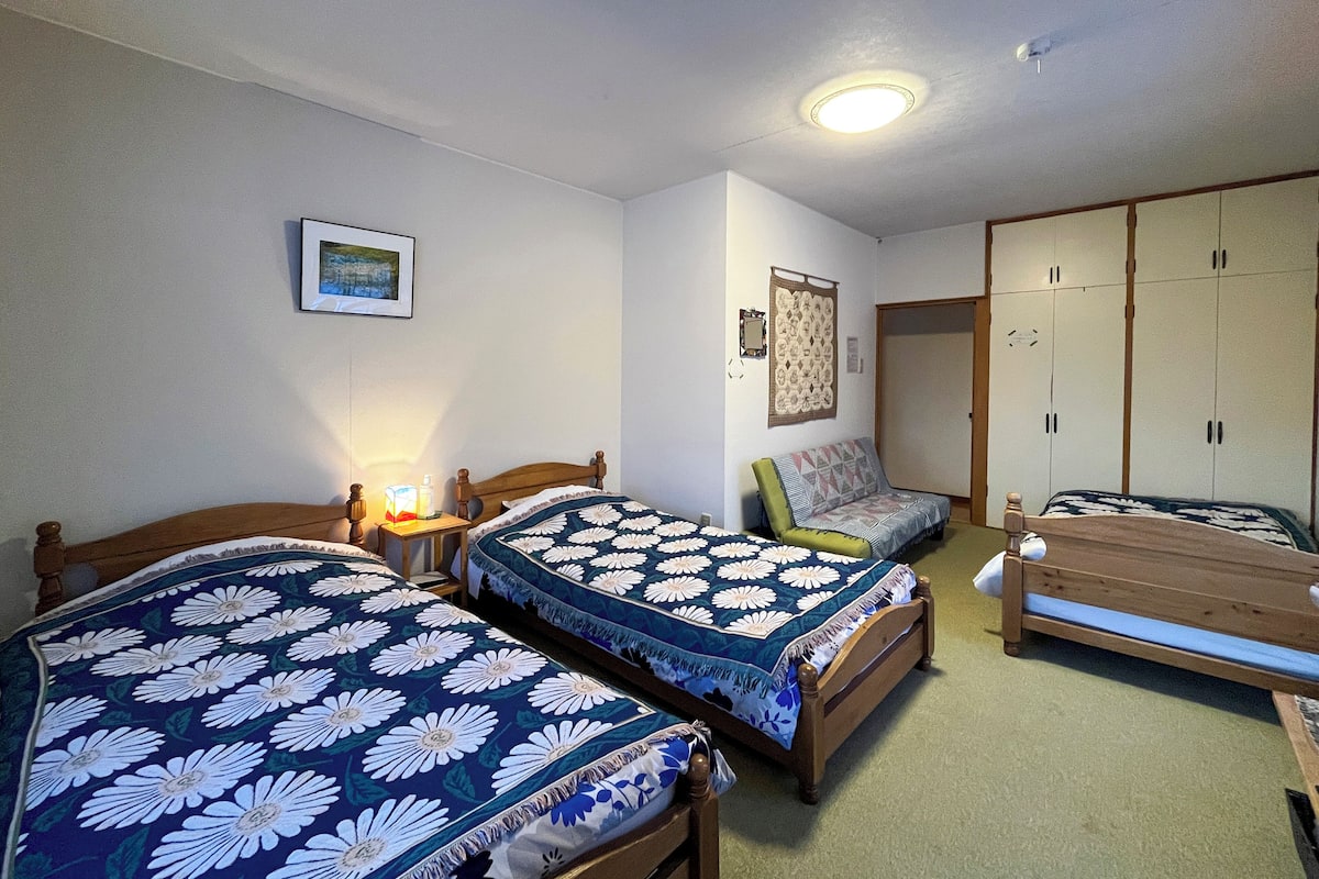 A bedroom with two single beds, a bedside table with a lamp, a chair, a wardrobe, and a framed picture on the wall.