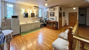 A compact kitchen with a microwave, sink, and cabinets. There is a wooden bench and a staircase leading to another level. - Pension Natsumi no Sato (Biei)