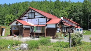 A two-story house with a red roof, wooden exterior, and a satellite dish. - Pension Natsumi no Sato (Biei)