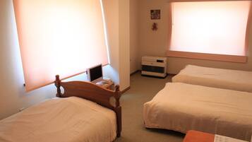 A hotel room with two single beds, a wooden headboard, a small desk with a computer, and a heater.