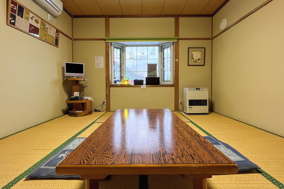 A tatami mat room with a wooden table, a television on a stand, a window with a view, and an air conditioning unit.