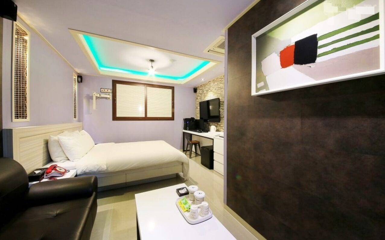 Una habitación de hotel con una cama, un escritorio, una silla, una mesa de centro y un televisor montado en la pared.