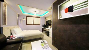 Una habitación de hotel con una cama, un escritorio, una silla, una mesa de centro y un televisor montado en la pared.