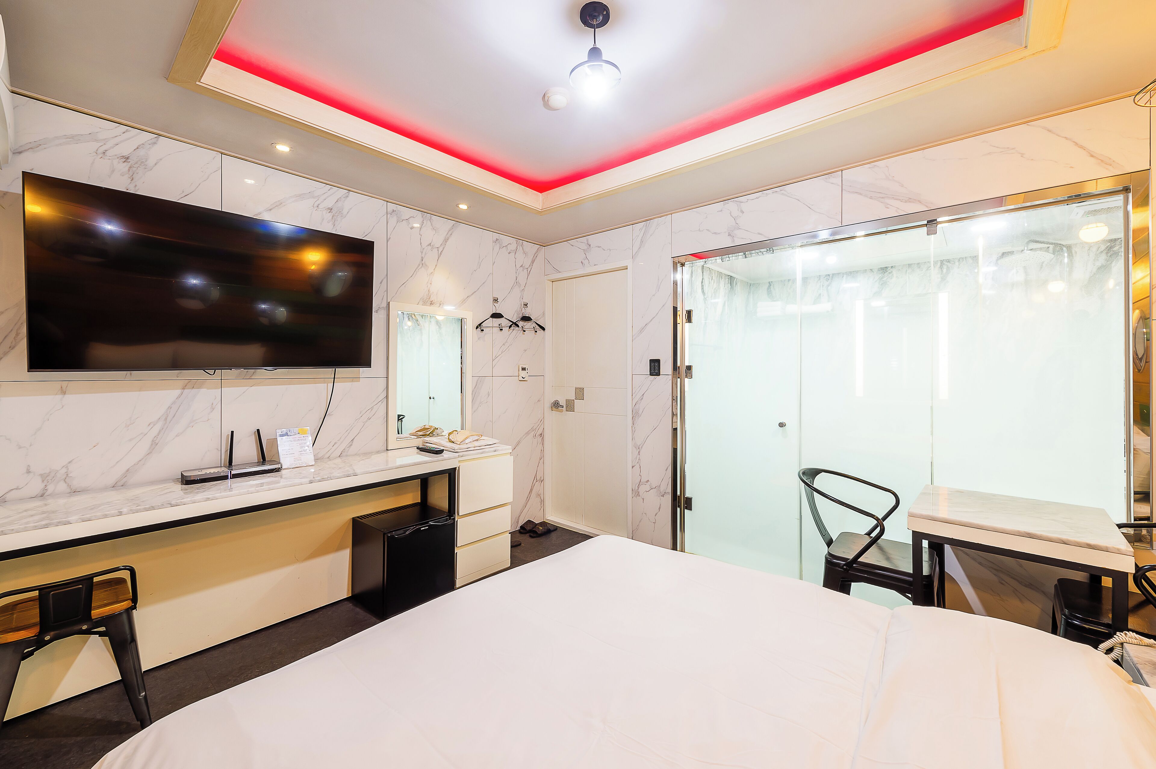 A modern hotel room with a large bed, a desk with a flat-screen TV, a vanity with a mirror, and a walk-in closet with a sliding door.