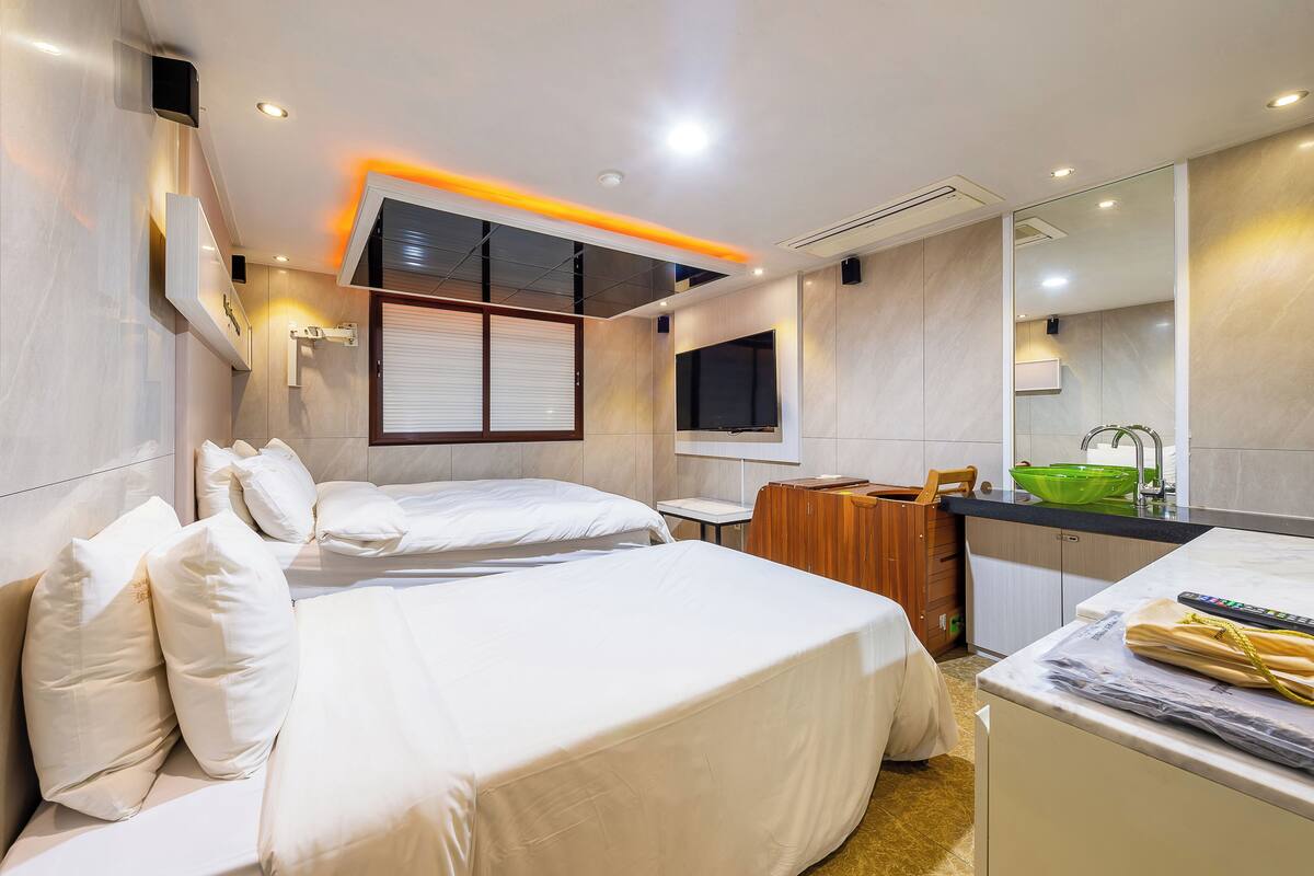 A hotel room with a bed, a desk, a mirror, and a bathroom with a sink and mirror.