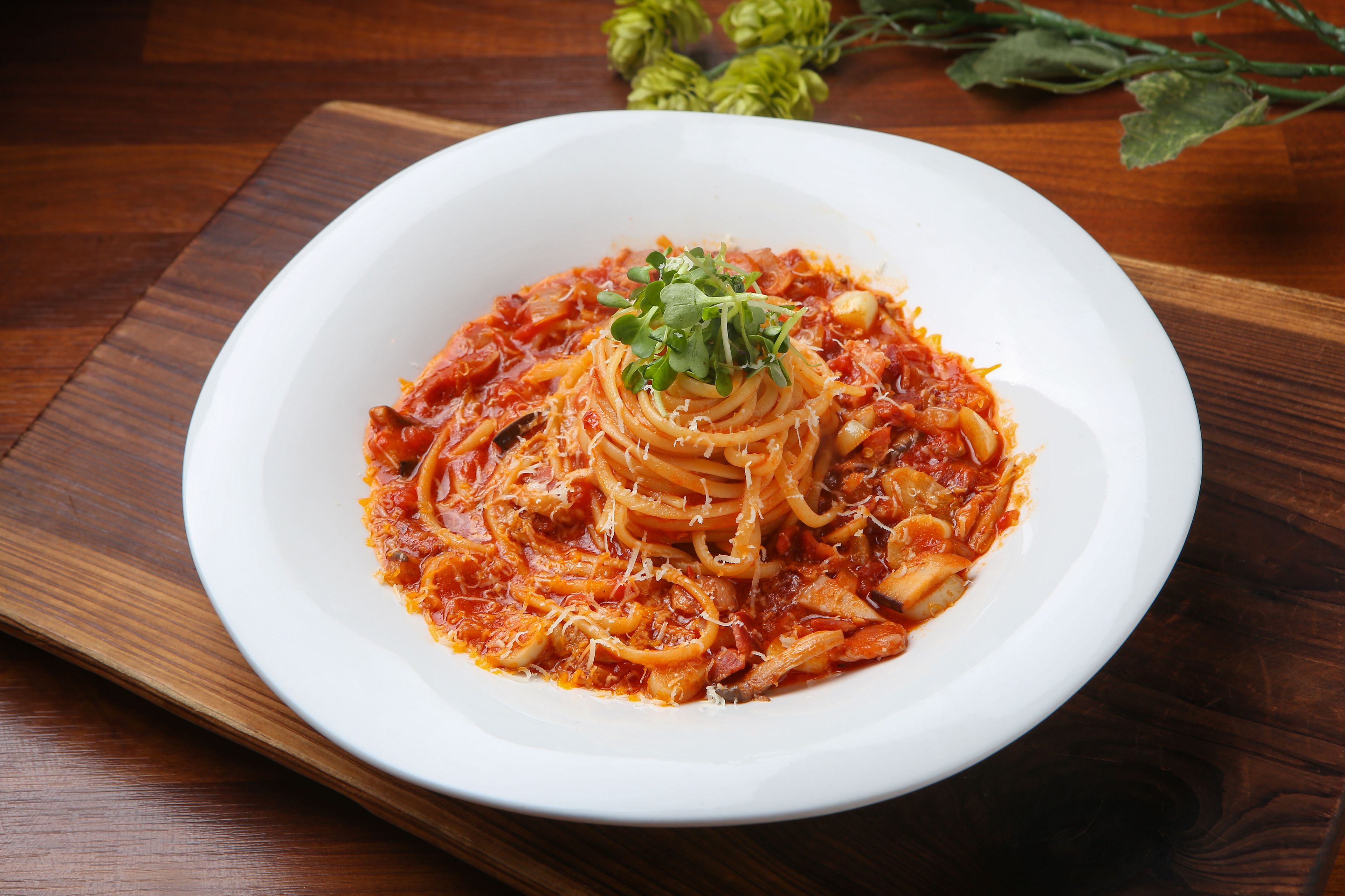 A white plate of spaghetti with tomato sauce and cheese on a wooden table.