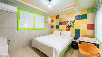 A modern bedroom with a bed, a window with blinds, a colorful wall, and a small table with a chair.