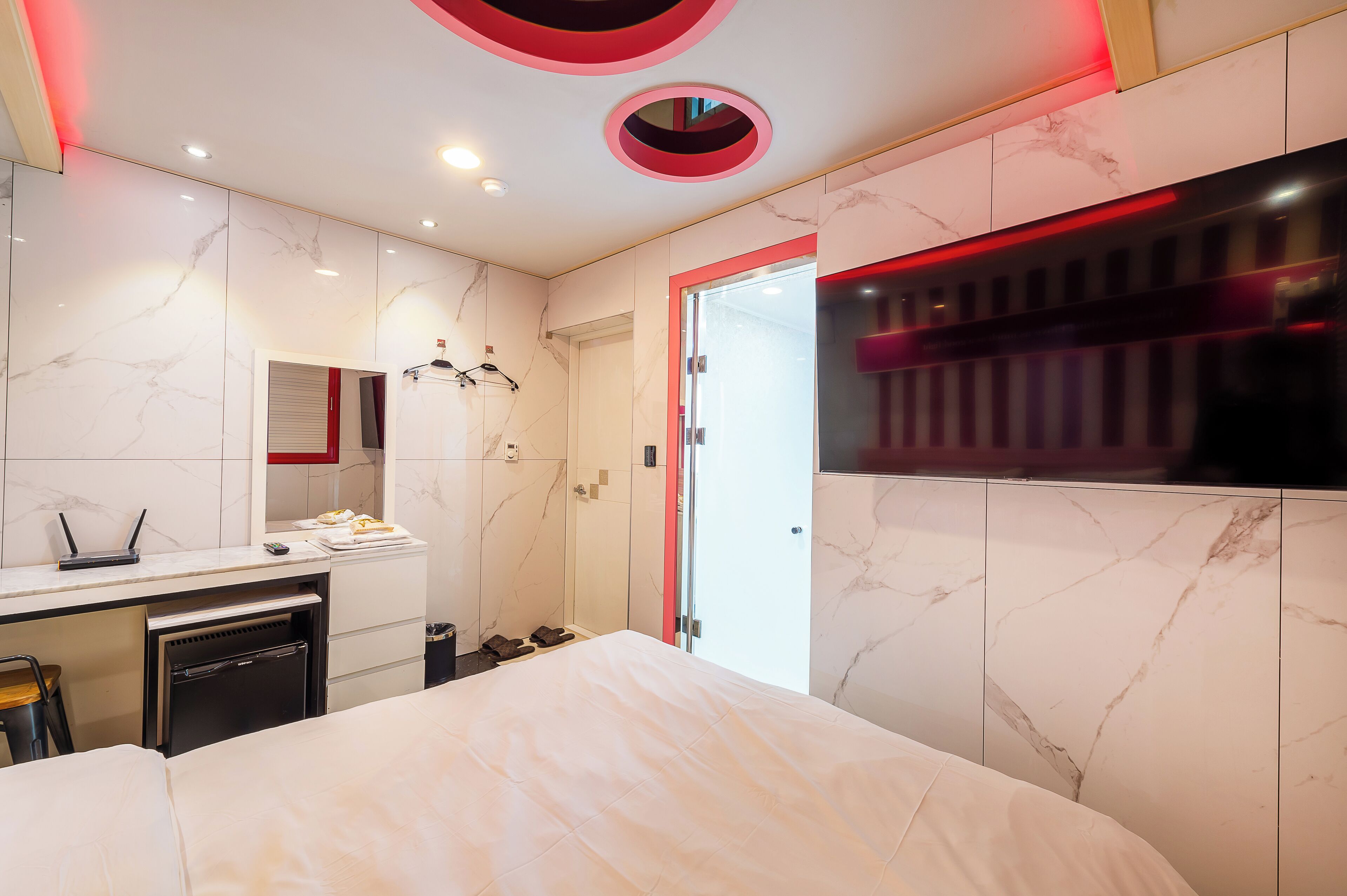 A modern hotel room with a marble wall, a bed, a desk with a laptop, and a minibar.