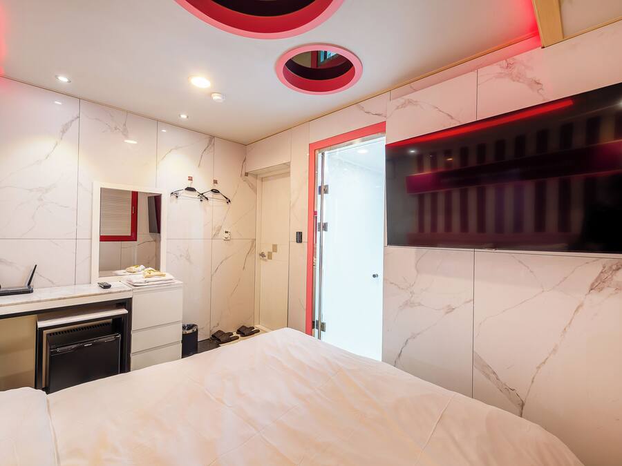 A modern hotel room with a marble wall, a bed, a desk with a laptop, and a minibar.