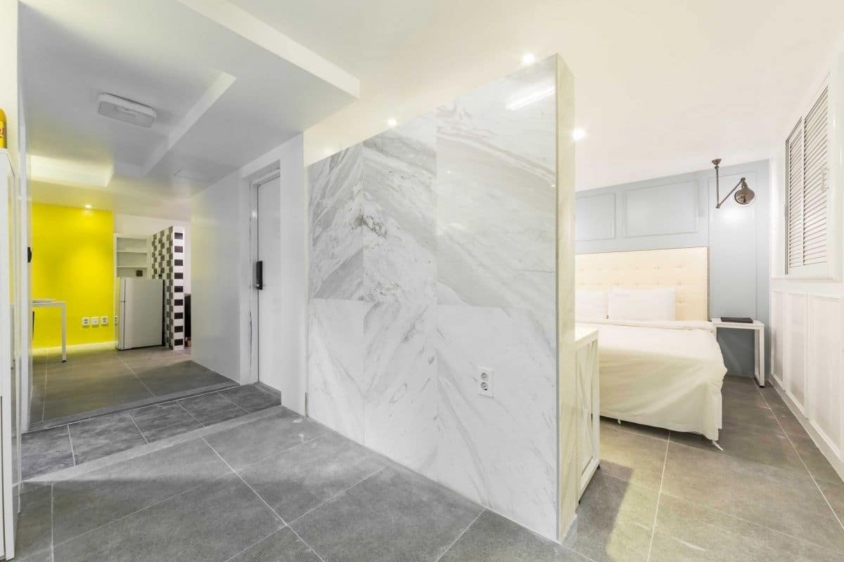 A hotel room with a marble partition, a bed, a bedside table, and a window with blinds.