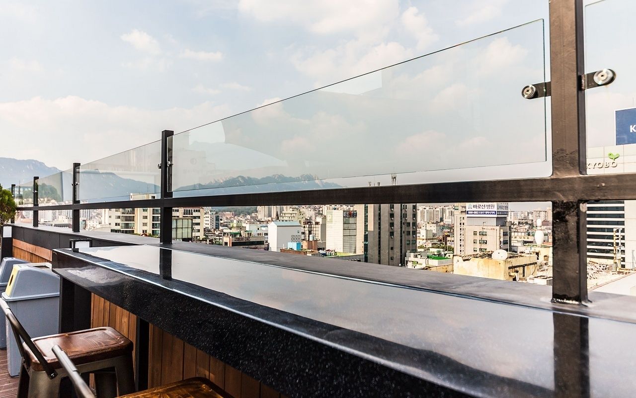 A rooftop bar with a glass railing overlooking a cityscape with mountains in the background.