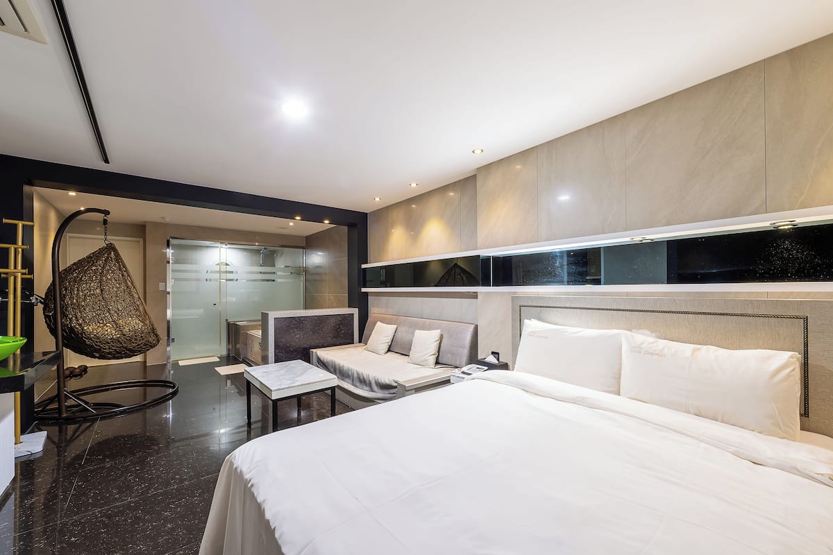 A modern hotel room with a large bed, a seating area, and a glass-enclosed shower.
