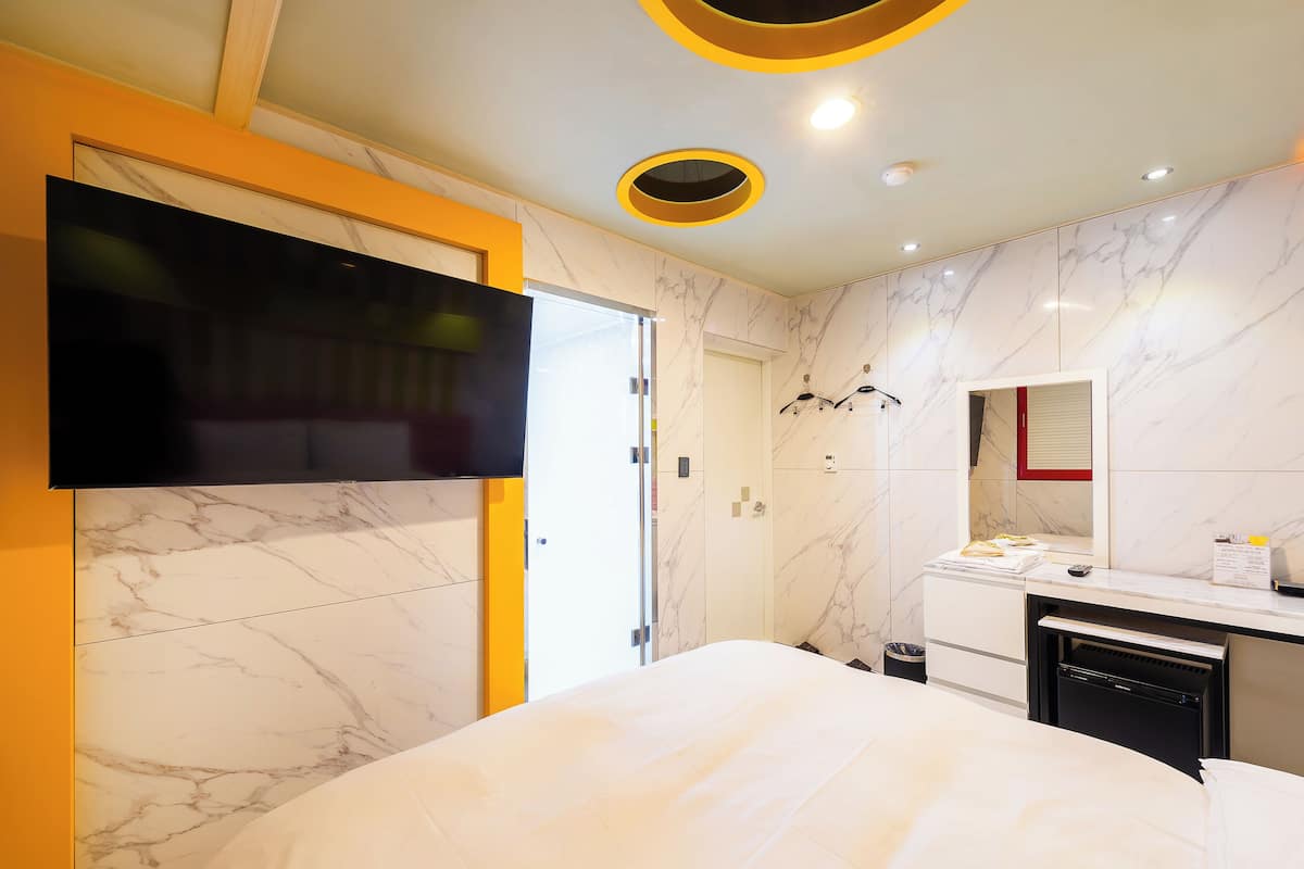 A modern hotel room with a large bed, a TV mounted on the wall, a mirror, and a small desk with a sink.
