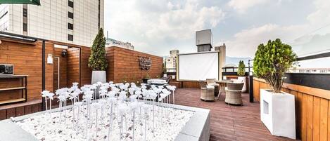 An outdoor rooftop terrace with a koi pond, wooden deck, seating areas, and a view of the cityscape.