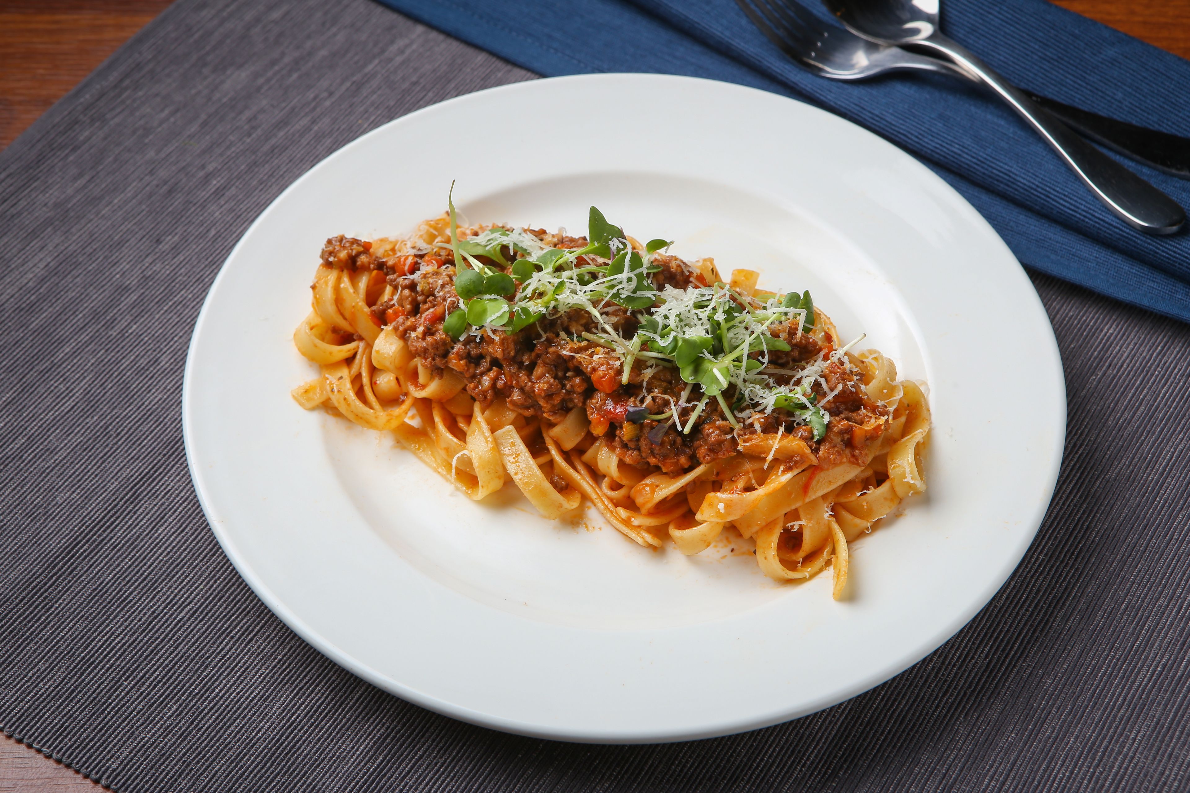 Un piatto di pasta con ragù e verdure su un piatto bianco.
