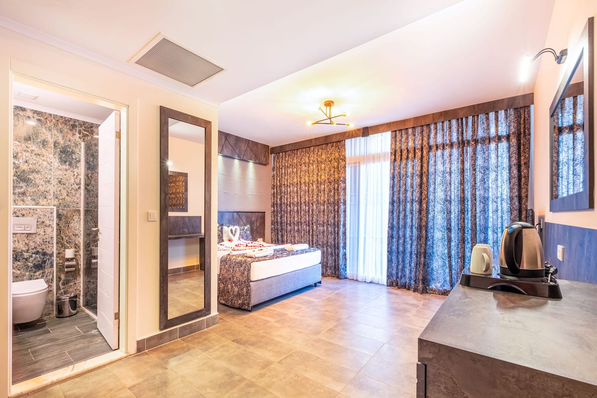 Moderni hotellihuone, jossa on suuri sänky, marmorilla verhoiltu suihku ja suuret ikkunat, joista avautuu näkymä kaupunkiin.