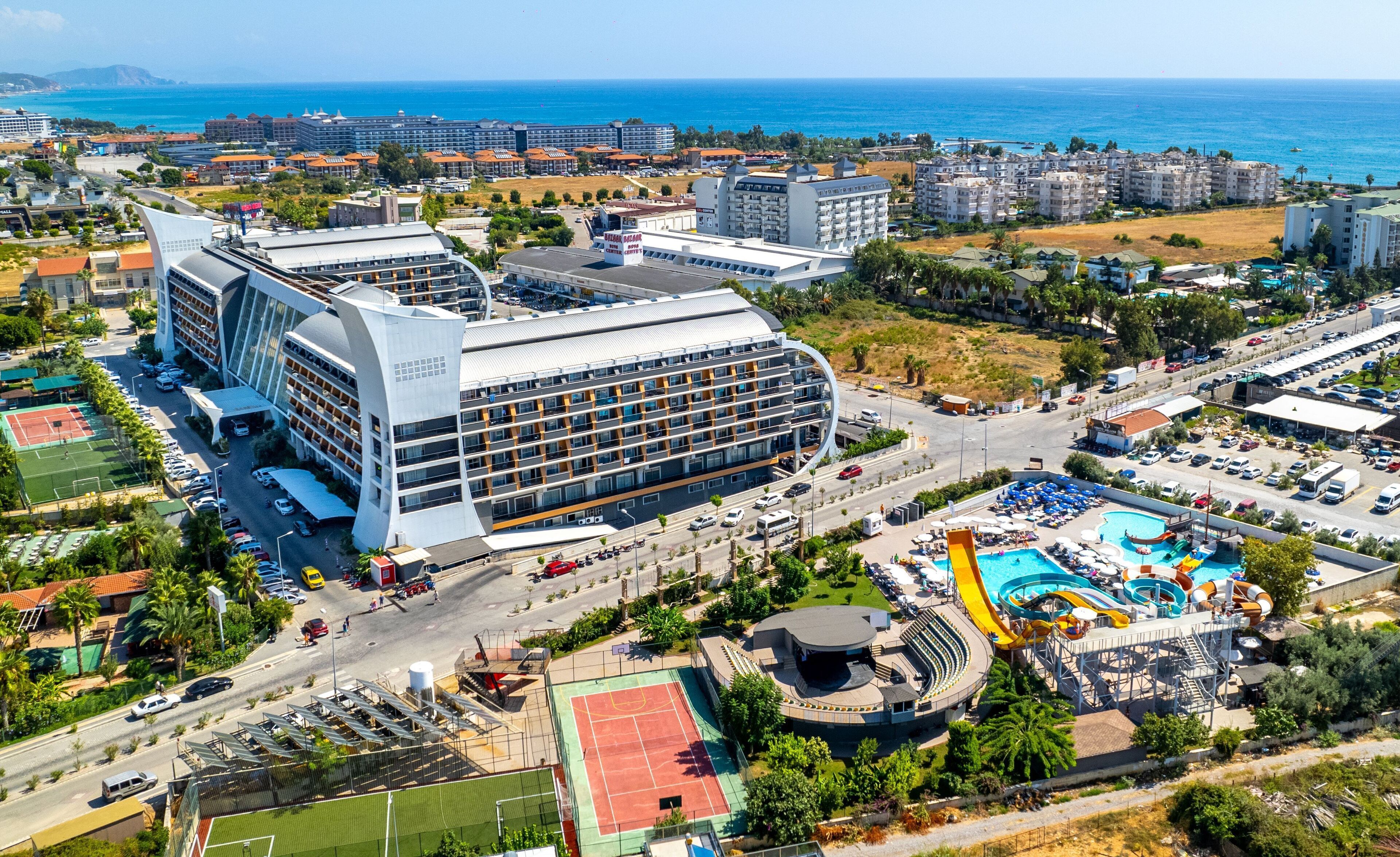 Un hotel moderno con fachada curva, varios pisos y zona de piscina en la azotea.