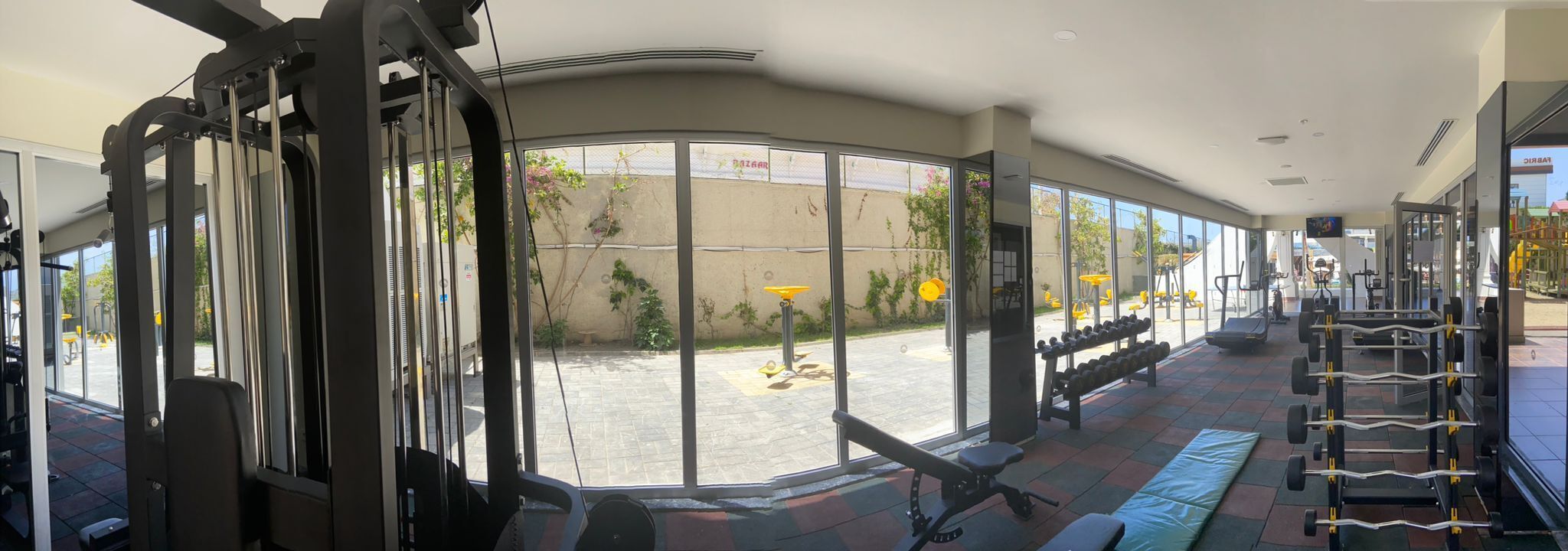 Un gimnasio con amplias ventanas, equipamiento de ejercicio y vistas al exterior.