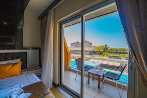A hotel room with a large window, a bed, a small table, and a chair.
