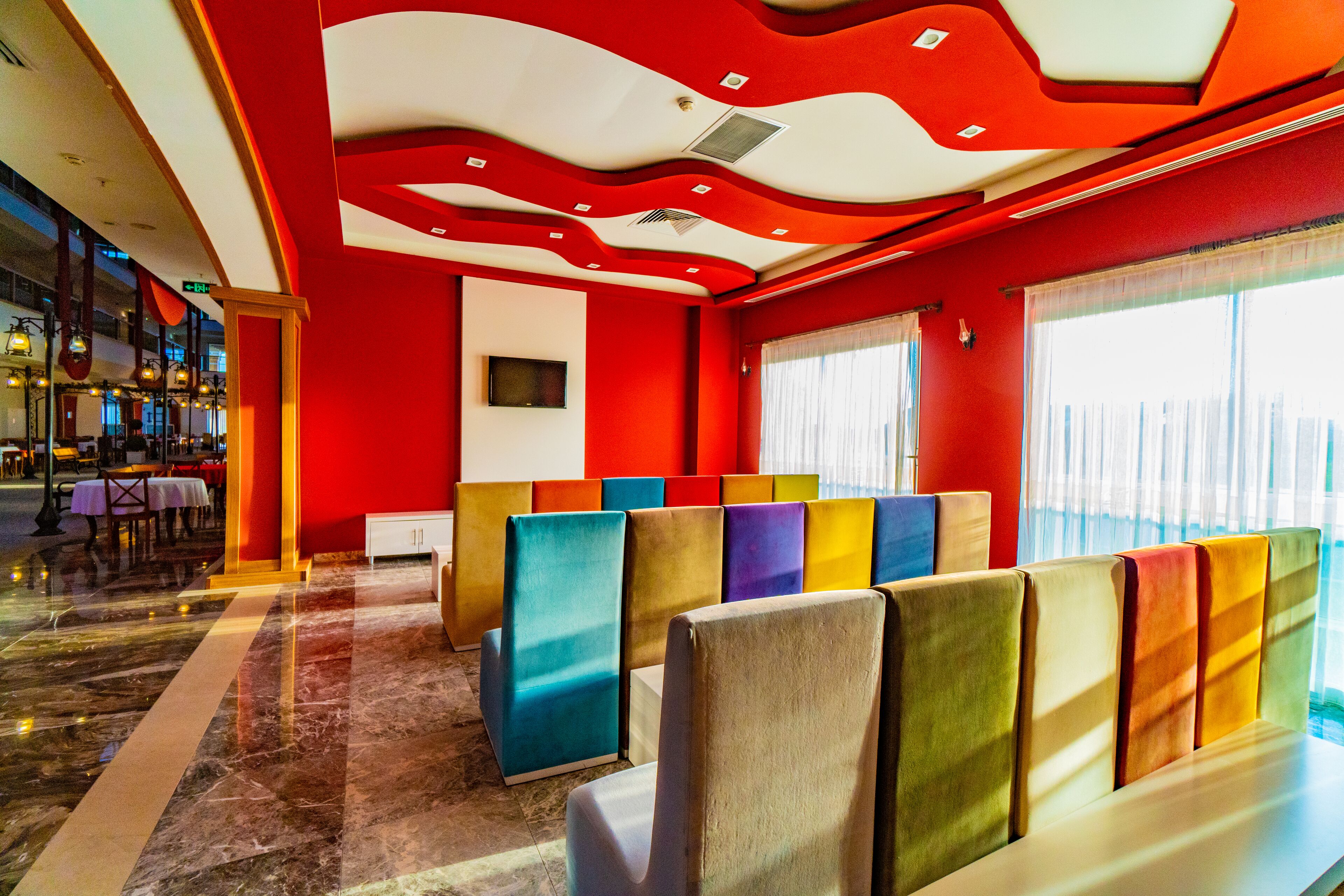A hotel lobby with a red and white color scheme, a seating area with colorful backrests, and a view of the city through large windows.