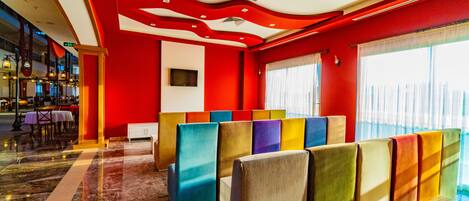 A hotel lobby with a red and white color scheme, a seating area with colorful backrests, and a view of the city through large windows.