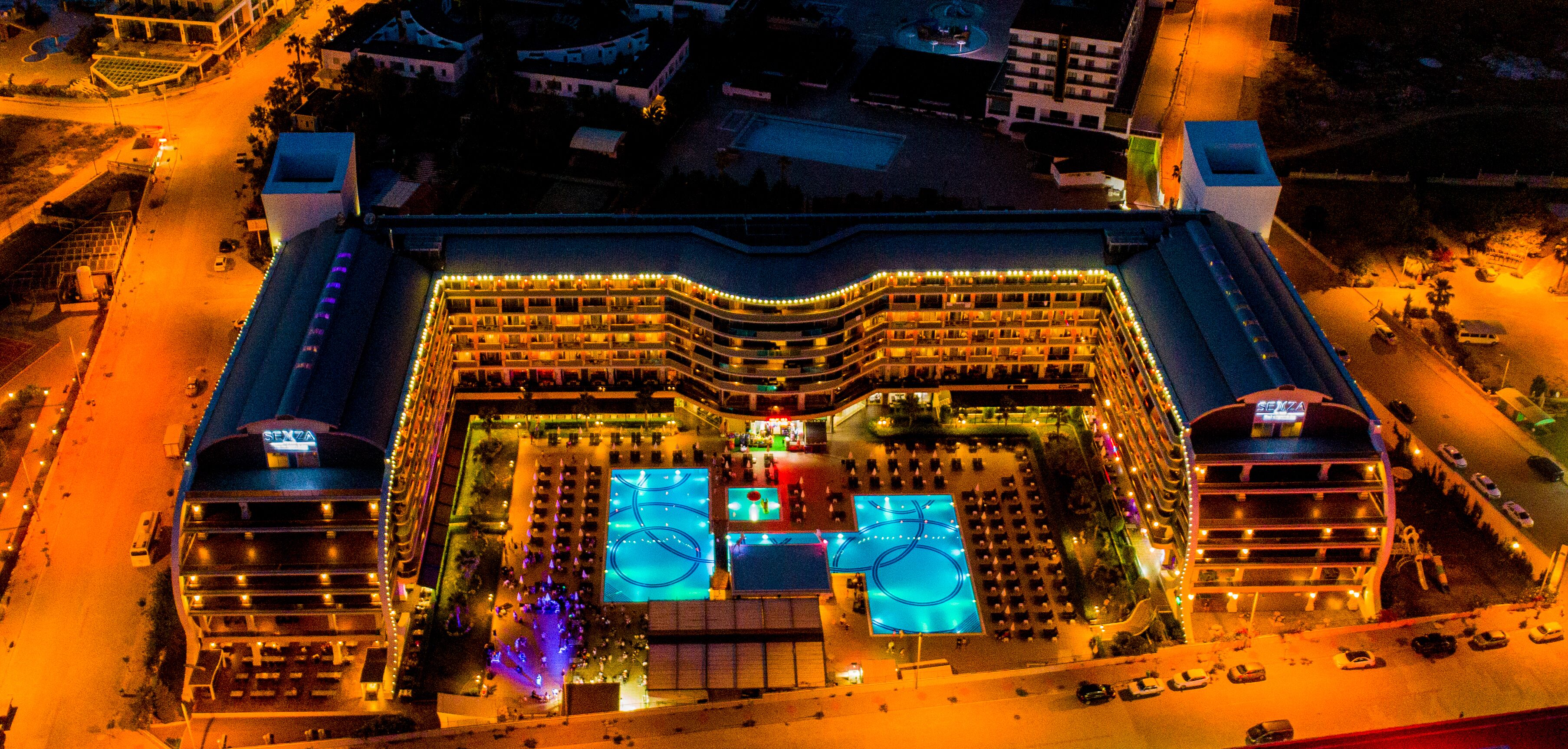 Vista aérea de un hotel con varios pisos, un patio central con piscina y un estacionamiento.