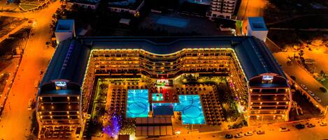 An aerial view of a hotel with multiple floors, a central courtyard with a swimming pool, and a parking area.