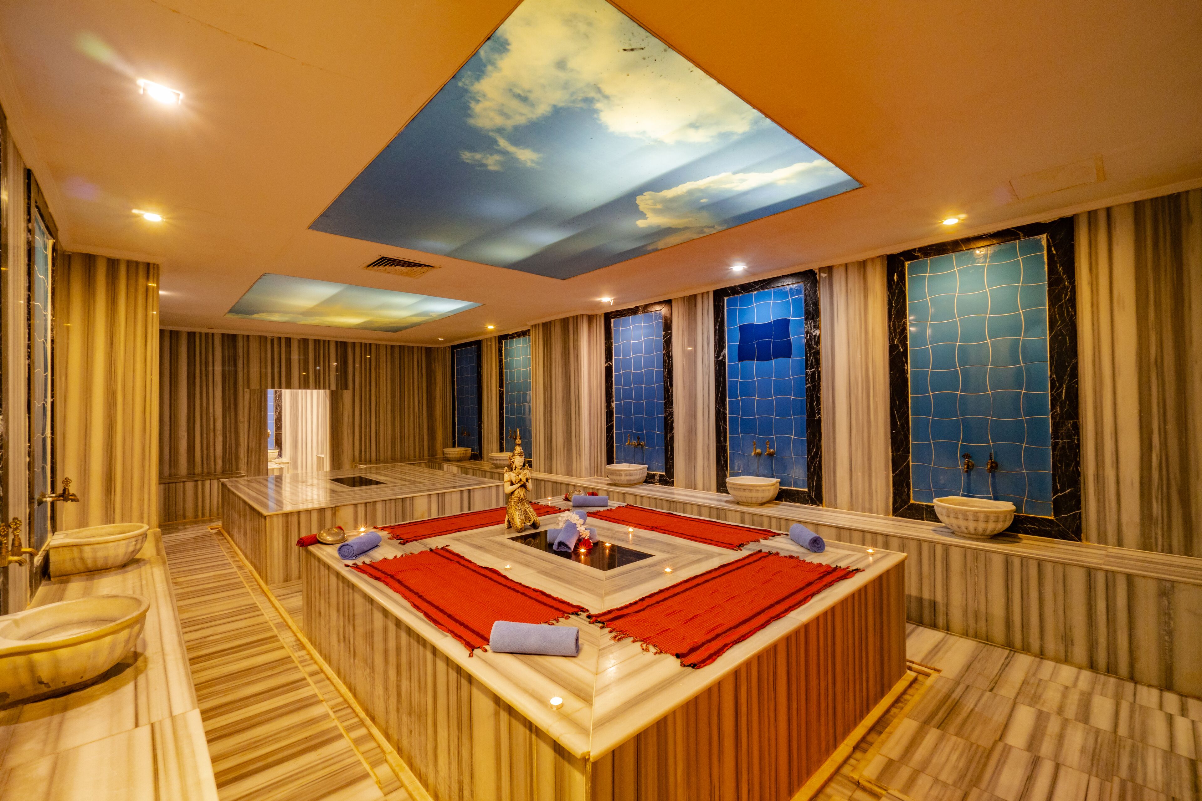 Un baño lujoso con un lavamanos grande en el centro, varios lavabos y un techo con diseño de nubes.