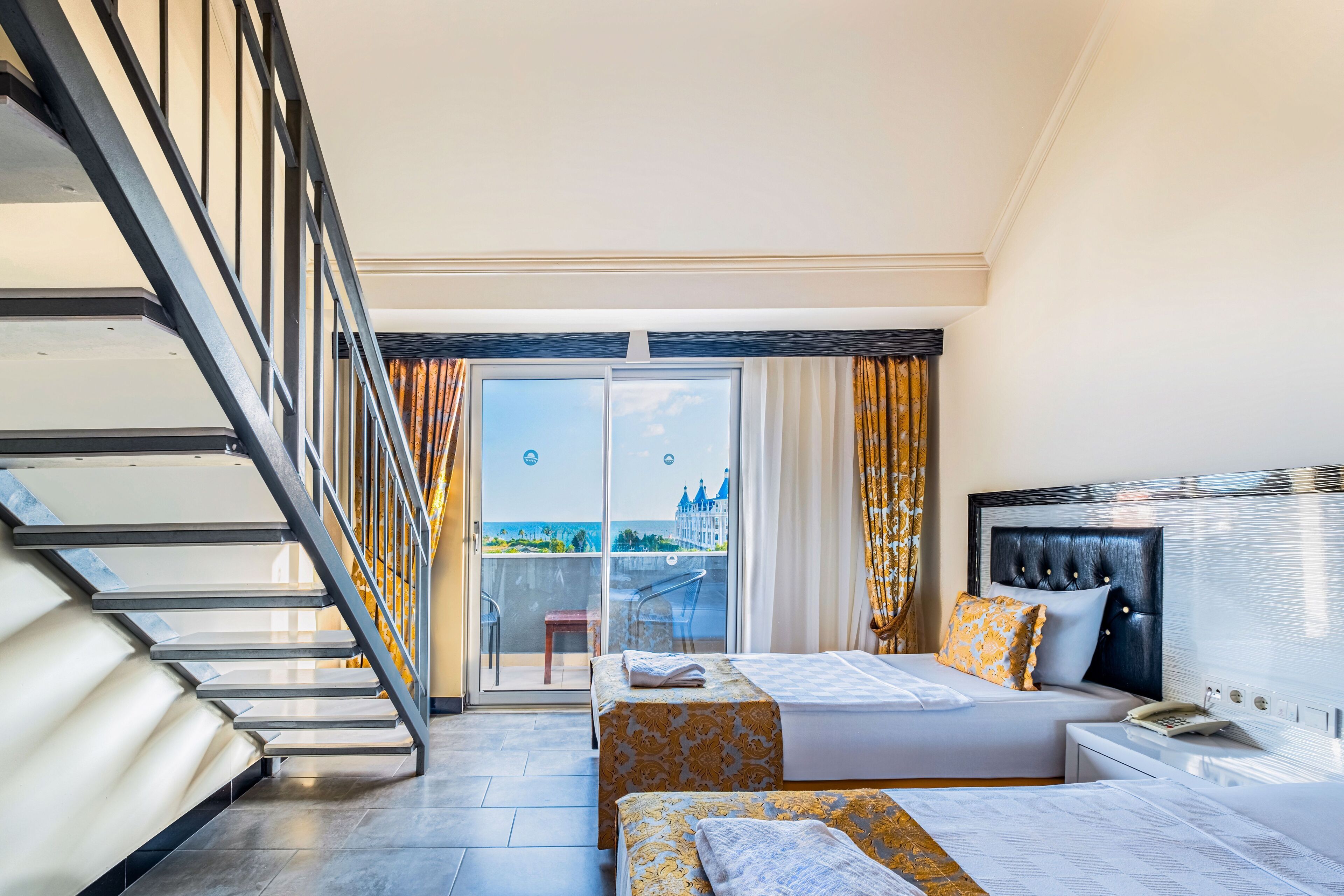 A hotel room with a bed, bedside table, and a view of the city through a balcony.
