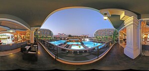 A panoramic view of a hotel atrium with a central pool, multiple balconies, and a view of the surrounding cityscape.