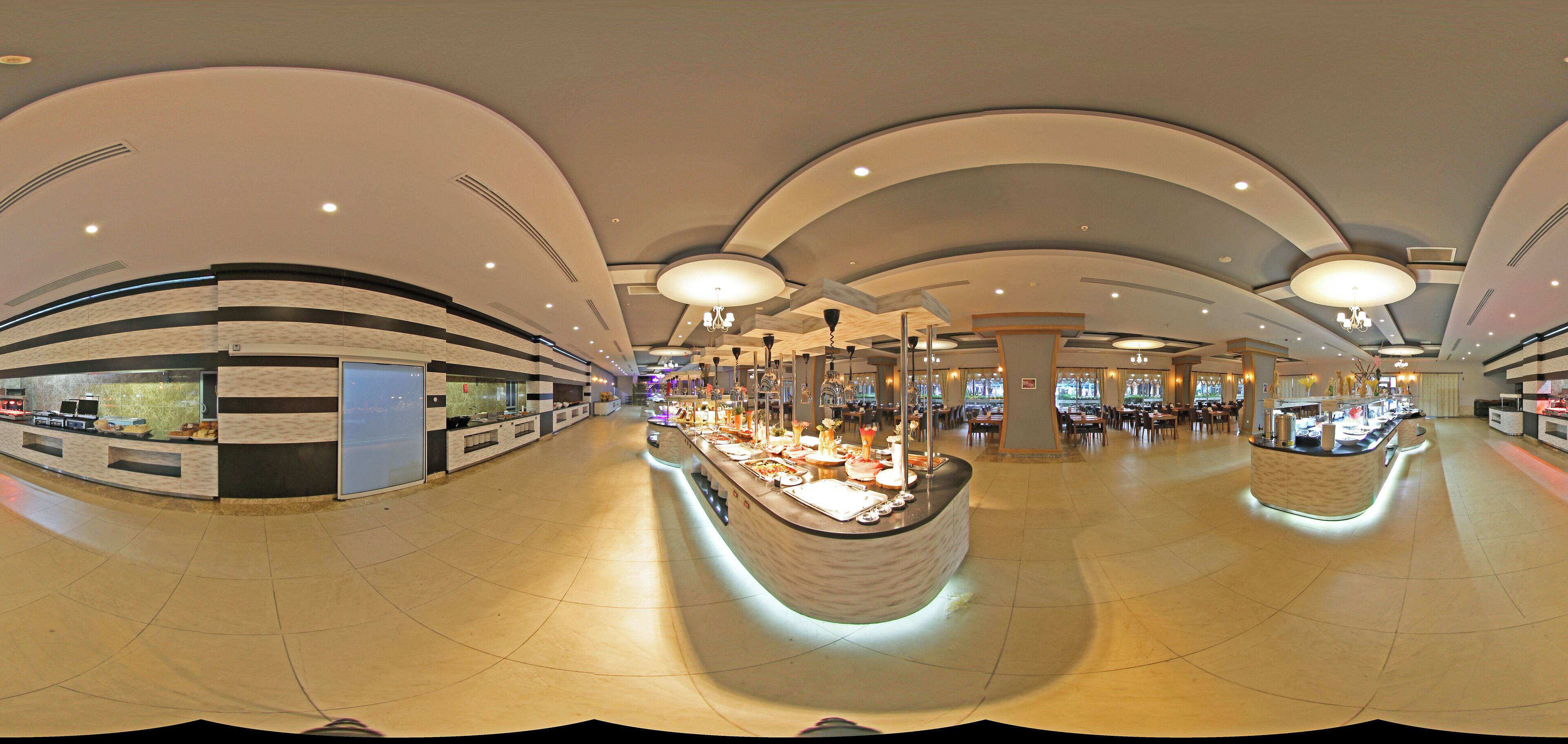 Un hall d’hôtel spacieux et moderne, doté de plafonds incurvés, d’un îlot central où est installé un buffet, et d’un sol carrelé et impeccable.