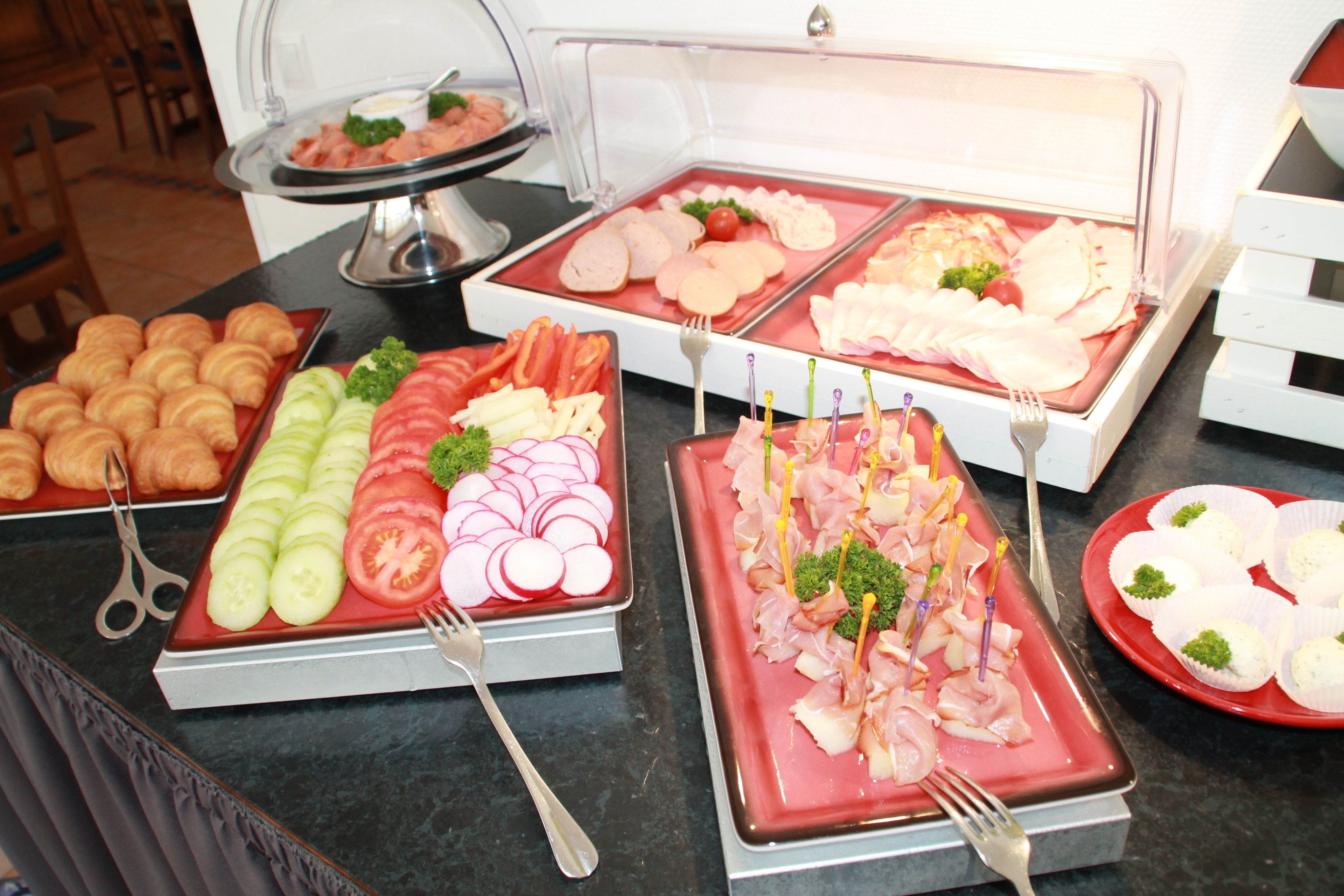 A buffet with various food items including sliced vegetables, meats, and pastries.