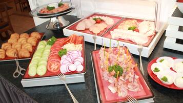 A buffet with various food items including sliced vegetables, meats, and pastries.