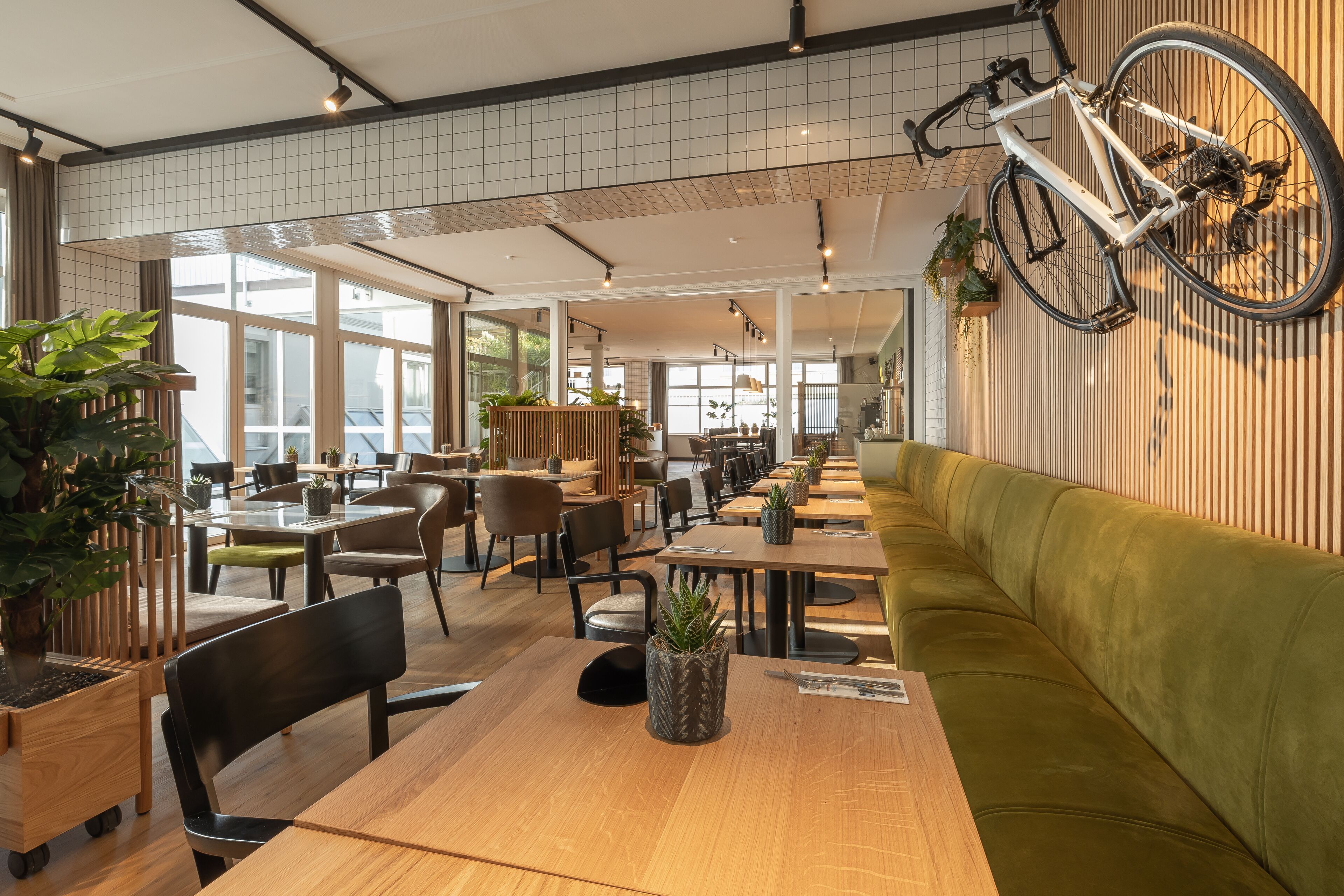 Una cafetería amplia con mesas de madera, asientos acolchados verdes y una bicicleta colgada en la pared.