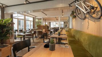 Una cafetería amplia con mesas de madera, asientos acolchados verdes y una bicicleta colgada en la pared.