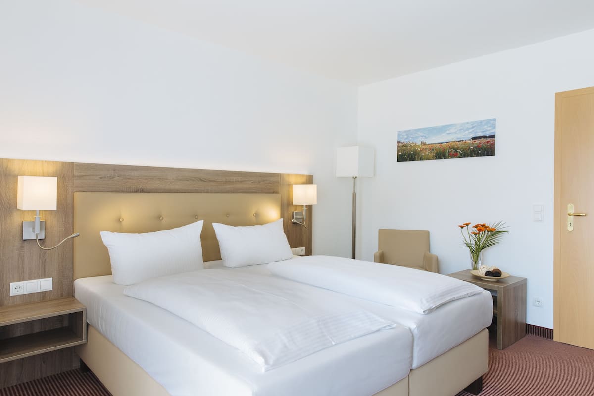 Ett hotellrum med en stor säng, sänglampor, ett nattduksbord, ett litet bord med en vas med blommor och en tavla på väggen.