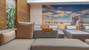 A modern lounge area with a beach mural, cushioned seating, and wooden paneling. - Hotel Meerzeit Binz (Binz)