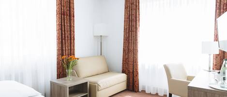 A hotel room with a bed, a sofa, a desk, and a chair.