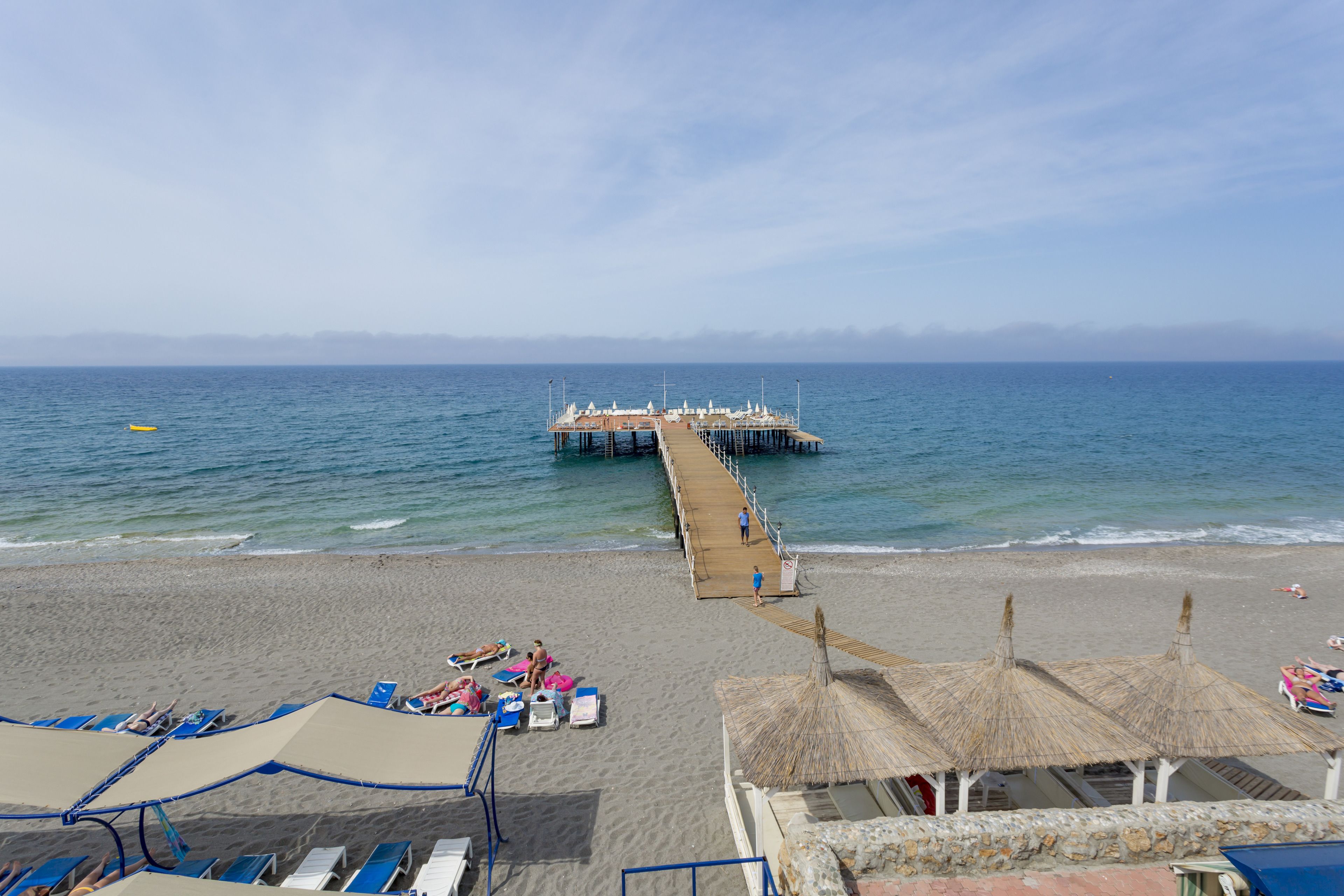 A beach with a pier extending into the sea, sun loungers, and umbrellas.