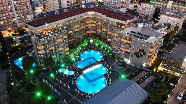 Un hotel de varios pisos con un patio central que cuenta con dos piscinas, rodeado de balcones y zonas de estar al aire libre.