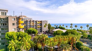 Un hotel con varios pisos, balcones y una zona de piscina rodeada de palmeras.