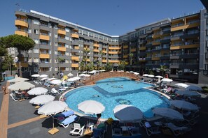 Un hotel con piscina central rodeada de tumbonas y sombrillas, con varios balcones y un cielo despejado.