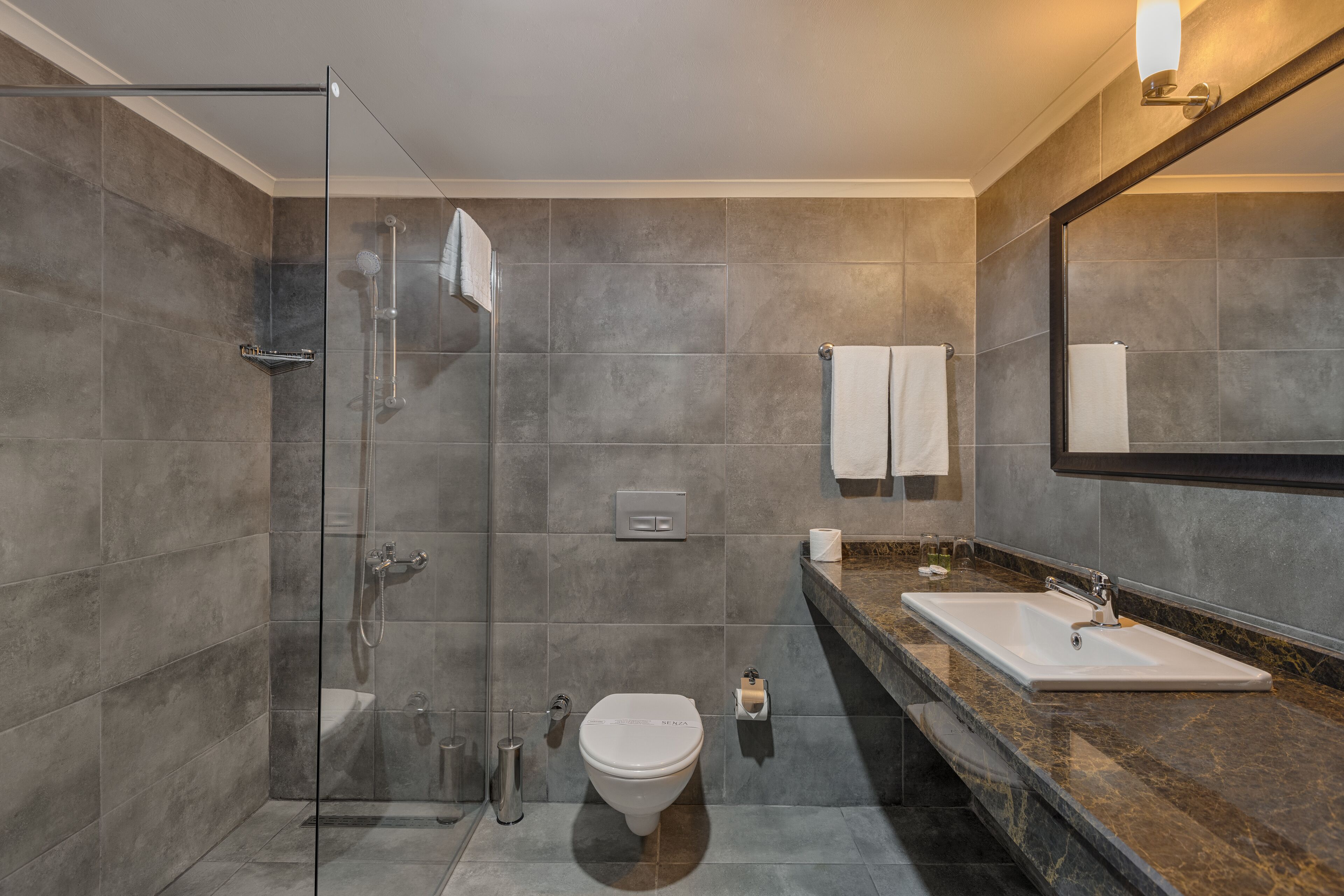 Un baño moderno con ducha envuelta en vidrio, inodoro y lavamanos con encimera de mármol.